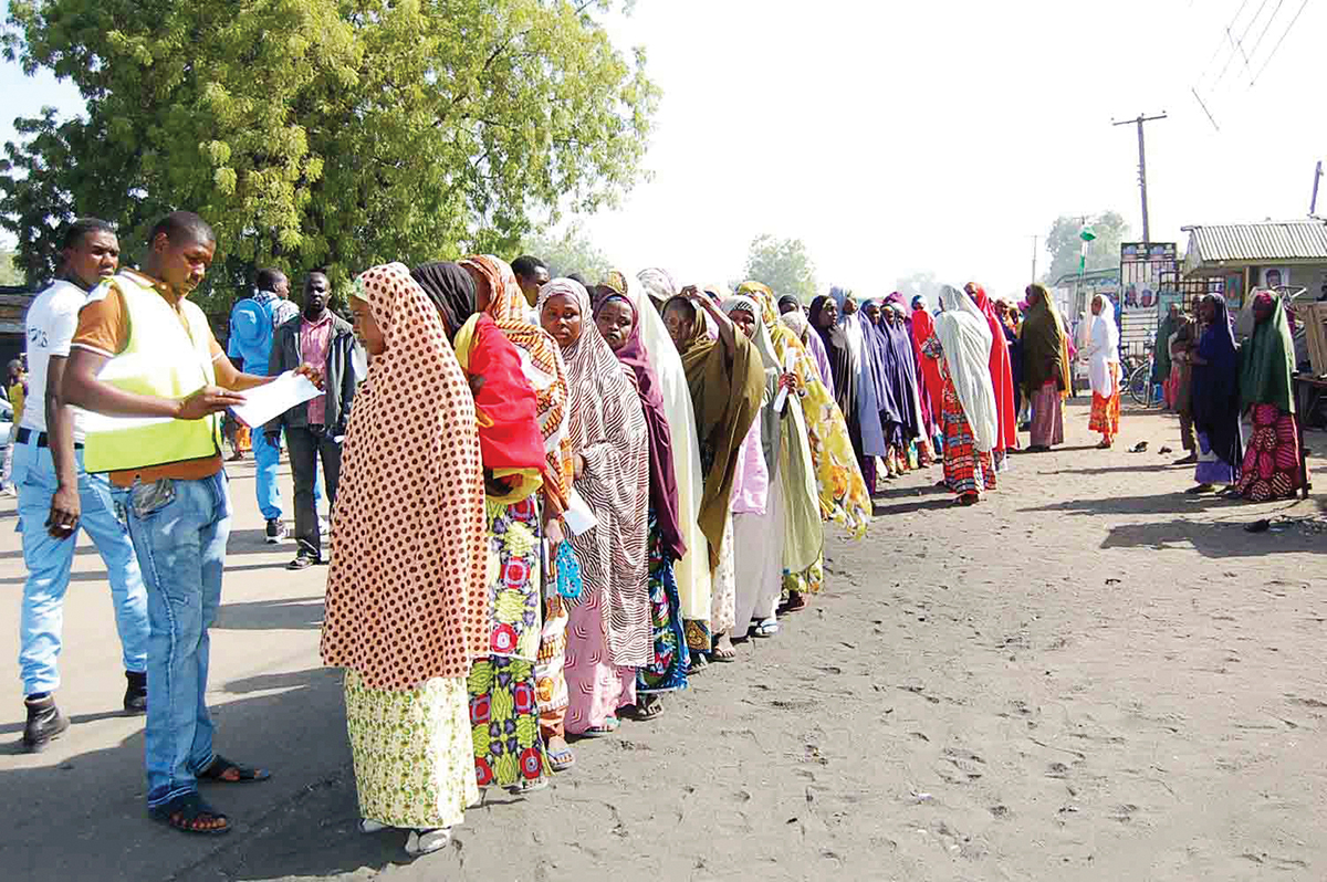 Displaced people fleeing from violence wait in line to receive relief materials at a camp for displaced people camp in Borno State